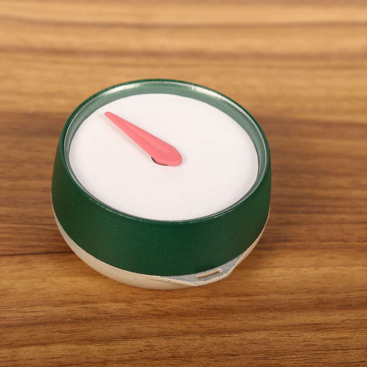 Het Kompas op een houten tafel: een rond, groen kompas met een witte wijzerplaat en één rode pijl